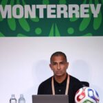 Man at a press conference desk with a laptop two water bottles and a colorful soccer ball MONTERREY banner behind  trybalnews