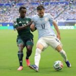 Two soccer players contest the ball on a green field one in light blue with number 17 and the other in dark green as a crowded stadium watches  trybalnews