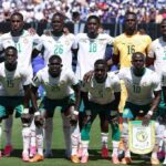 Senegal national football team posing on a sunlit pitch in white jerseys standing and kneeling for a pre match team photo with a banner in front  trybalnews