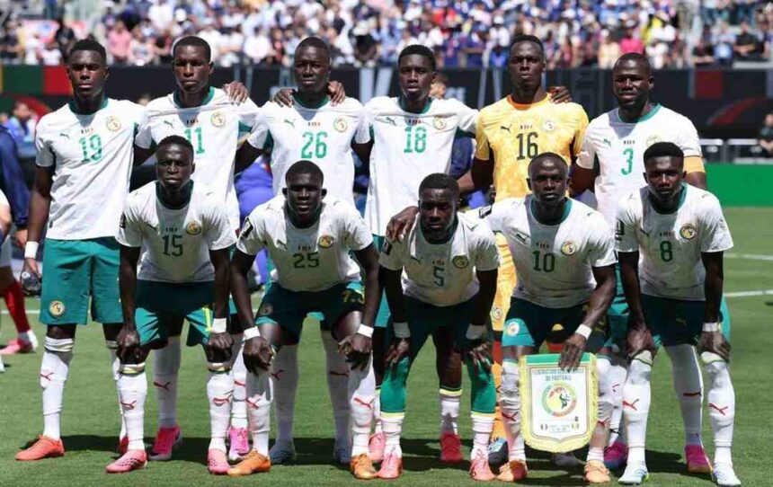 Senegal national football team posing on a sunlit pitch in white jerseys standing and kneeling for a pre match team photo with a banner in front  trybalnews
