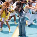 Burna Boy in a blue denim suit sings into a microphone on a turquoise stage surrounded by dancers in white and yellow outfits at the FIFA World Cup Opening Ceremony  trybalnews