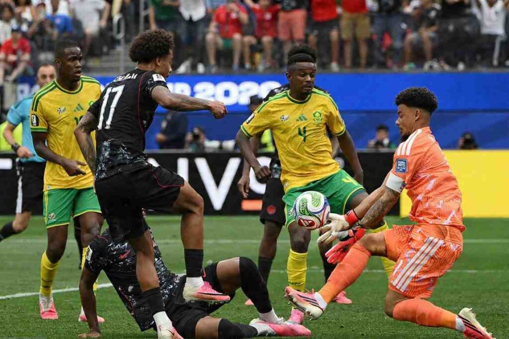 South Africa v Canada Trybal News South Africa goalkeeper Ronwen Williams wearing an orange kit with white armband and number 1 dives to his right to make a save Canada midfielder Tajon Buchanan in a black kit with red trim and number 17 challenges for the ball near the goal line with his leg raised South Africa defenders in yellow and green kits watch the action The 2026 FIFA World Cup Round of 32 match between South Africa and Canada was played on June 28 2026 at Los Angeles Stadium in Inglewood A packed crowd is visible in the stands behind the goal trybalnews