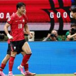 Two soccer players in red uniforms celebrate on the field as photographers film in the background  trybalnews