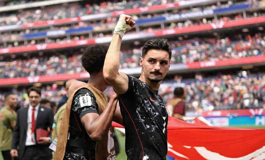 Canada midfielder Stephen Eustaquio wearing a black speckled kit with red trim and number 7 celebrates with a raised right fist His right wrist is wrapped in white tape A teammate in a brown training vest puts a hand on Eustaquios shoulder A large Canadian flag with a red maple leaf is visible behind them The 2026 FIFA World Cup Round of 32 match between South Africa and Canada was played on June 28 2026 at Los Angeles Stadium in Inglewood California with Canada advancing to the Round of 16 A packed crowd fills the red and blue stadium stands in the background  trybalnews