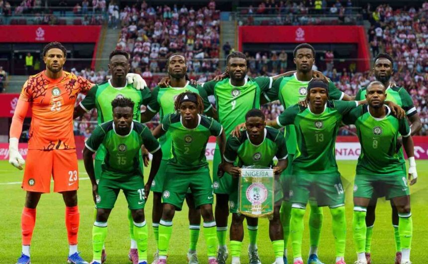 Nigeria national football team players pose for a group photo on the pitch green kits with the goalkeeper in orange on the left crowd in the stands behind them  trybalnews