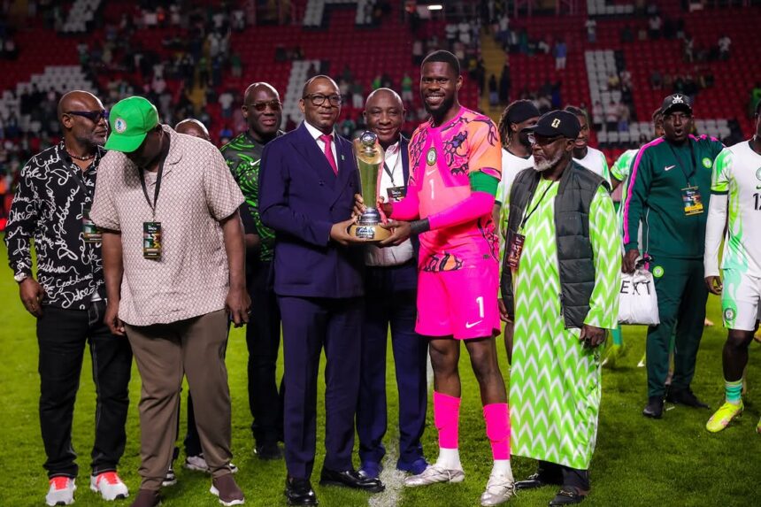 Soccer players and officials pose on a stadium field as a pink clad goalkeeper receives a trophy from an official in a suit  trybalnews