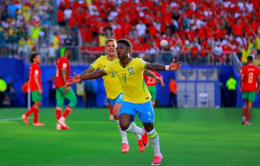 Brazilian soccer player in yellow jersey 7 celebrates with arms outstretched on a green pitch as teammates run by crowd in red in the stands behind him  trybalnews