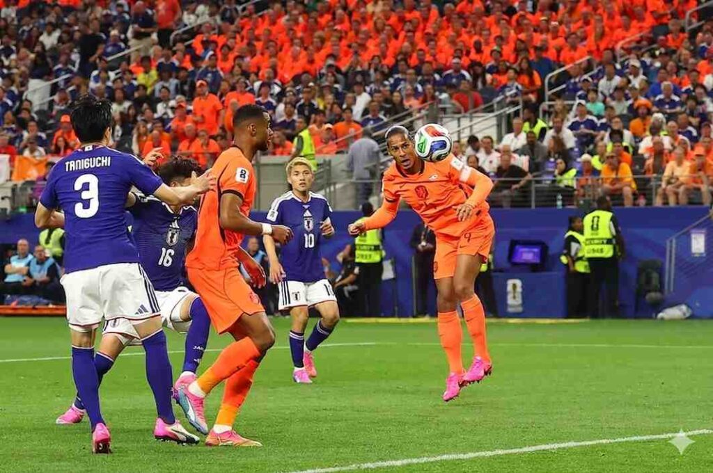VirgilVanDijk Trybal News Virgi Van Dijk leaps to head the ball during a match as Japan players crowd around on a green field with an Netherlands crowd in the stands trybalnews