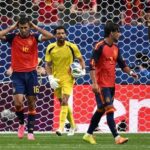Soccer scene at the goalmouth goalkeeper in yellow holding the ball two players in red and blue nearby and an opponent in white nearby with the net in the background  trybalnews