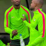 Two athletes in neon green training tops with pink stripes talk beside a water bottle during practice  trybalnews