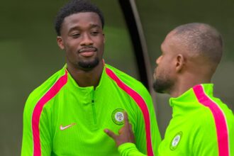 Two athletes in neon green training tops with pink stripes talk beside a water bottle during practice.