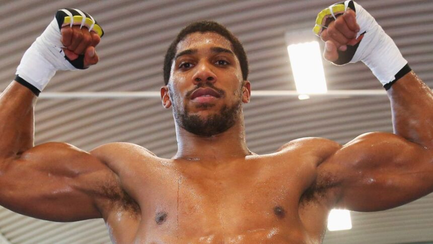 Male fighter with white hand wraps raises his clenched fists above his head in a gym sweat on his torso looking forward in a moment of victory  trybalnews