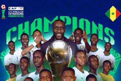 Senegal U-17 football team players pose with a large trophy and the word 'Champions' in the background, celebrating the CAF U-17 Africa Cup of Nations 2017.