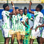 Group of female soccer players in white and green uniforms celebrate with raised arms on a green field after a goal or win  trybalnews