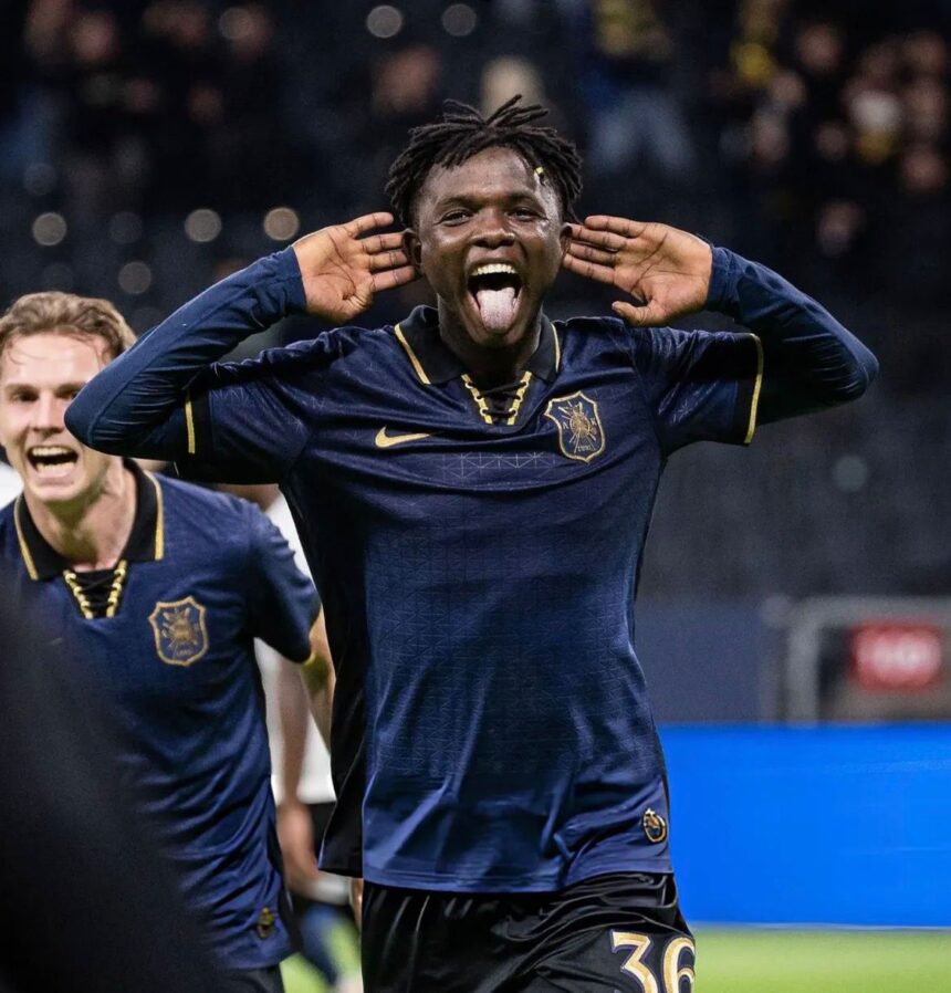Soccer player celebrating a goal with hands cupping his ears and tongue out wearing a navy kit with a gold crest and number 36  trybalnews
