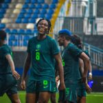 Soccer players in teal uniforms celebrate on a rainy field as stadium stands loom in the background  trybalnews
