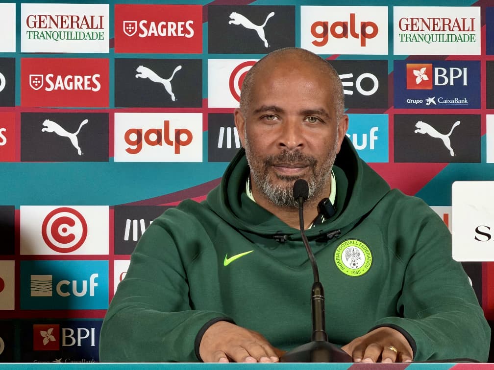 WhatsApp Image 20260609 at 160007 Trybal News Man in a green Nigeria football hoodie speaks at a press conference microphone in front of a sponsor filled backdrop trybalnews