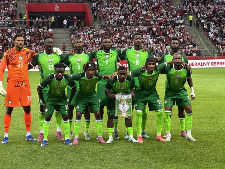 Nigeria national football team posing for a group photo on the pitch goalkeeper in orange on the left fans in stands behind them  trybalnews