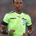 Soccer referee wearing a neon green kit with FIFA badge headset mic and black armbands running on the field  trybalnews