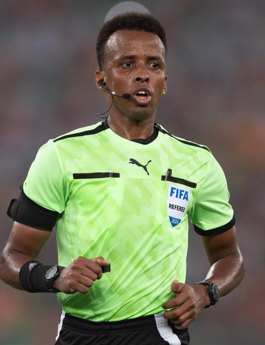Soccer referee wearing a neon green kit with FIFA badge headset mic and black armbands running on the field  trybalnews