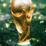 Golden World Cup trophy standing upright on green grass close up relief details visible on the sculpture  trybalnews