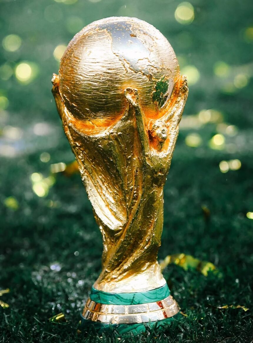 Golden World Cup trophy standing upright on green grass close up relief details visible on the sculpture  trybalnews