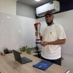 Man in a white t shirt and maroon cap holds a tall silver trophy in a modern office setting  trybalnews