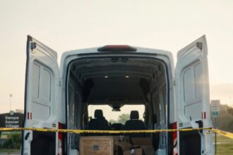 Back of a white van with doors open, yellow 'Police Do Not Cross' tape, and shoes, jerseys, and boxes on the pavement outside a crime-scene setup.