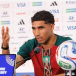 Male footballer at a press conference speaking into a microphone with a soccer ball on the table and a branded backdrop behind him  trybalnews