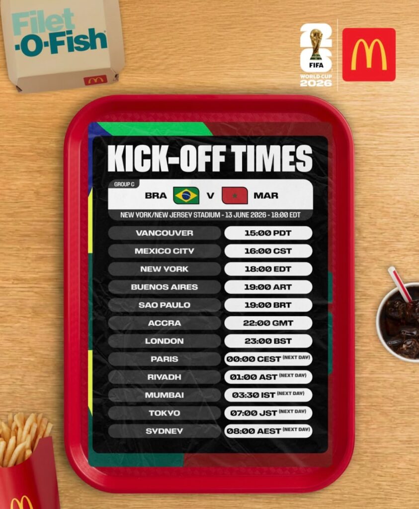 WhatsApp Image 20260613 at 093459 Trybal News Poster on a red tray labeled KICK OFF TIMES listing city names and match times for a FIFA World Cup event with a McDonalds and FIFA logo nearby on a wooden table trybalnews