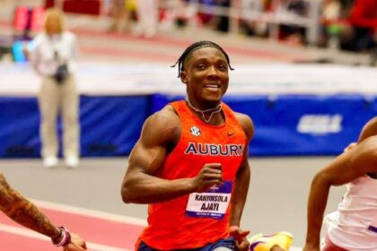 Auburn sprinter in red jersey running on a track, wearing a bib with the name Kanyinsola Ajayi