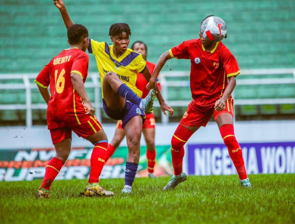 WhatsApp Image 20260614 at 180812 Trybal News Youth soccer players in red and yellow uniforms contest the ball on a grassy field with stadium seating in the background mid game action trybalnews