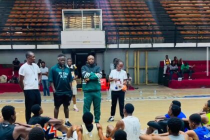 Basketball team seated on the court listening to coaches during a practice or meeting.