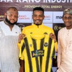 Three men pose together on a promotional backdrop the center man in a yellow and black jersey holds up a matching kit for display  trybalnews