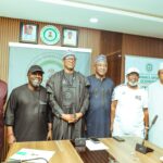 Group of six men in traditional Nigerian attire pose for a photo at a press conference standing behind a wooden table with microphones and banners in a formal room  trybalnews
