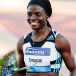 Smiling female sprinter on a track wearing a black and white Adidas top holding flowers after a race bib shows Amusan and Continental Tour Gold  trybalnews