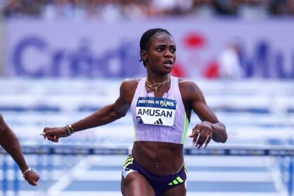 Female sprinter wearing a lavender kit crosses the track finish line with arms outstretched and a race bib reading AMUSAN.