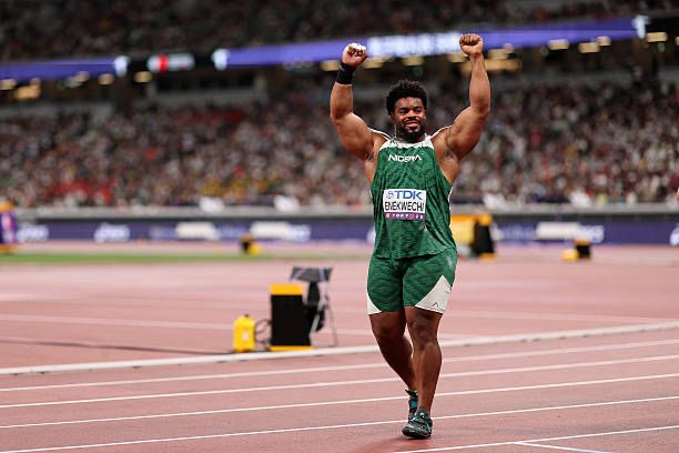 Track and field sprinter in a green uniform raises both arms in victory on the track as the stadium crowd watches  trybalnews