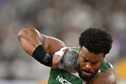 Nigerian hammer thrower in a green jersey preparing to throw the hammer in a stadium.