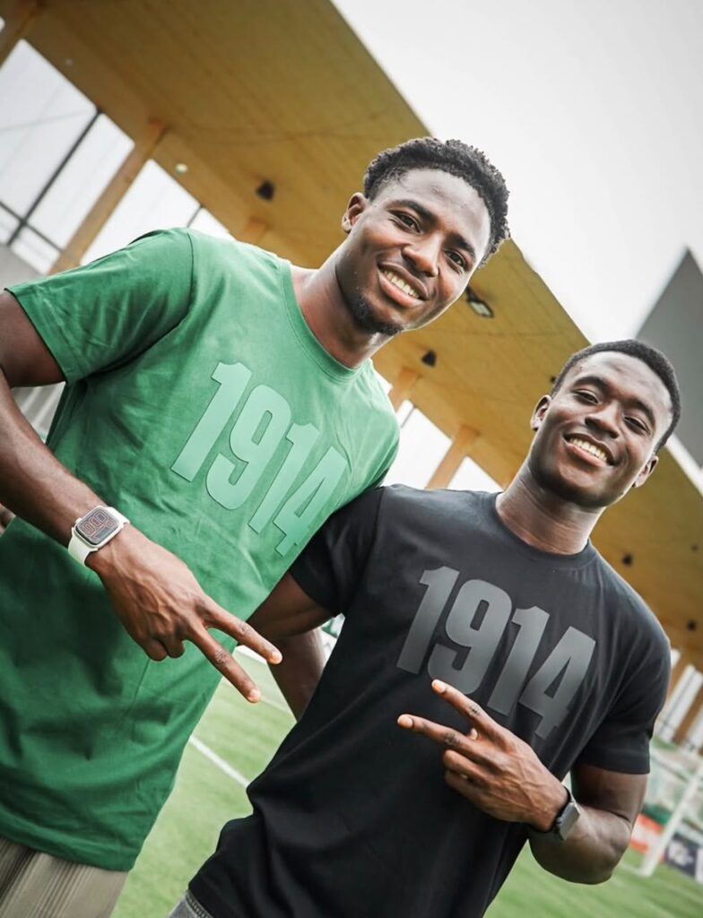 WhatsApp Image 20260630 at 194303 Trybal News Two young men posing on a sports field smiling and flashing peace signs wearing athletic tees with large numbers on them trybalnews
