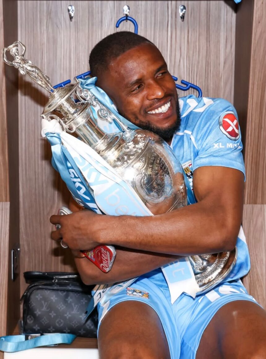 Athlete in a light blue sports kit hugs a large silver trophy in a locker room smiling  trybalnews