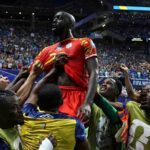 Congo DR forward Yoane Wissa wearing a red kit with yellow details and number 2 is lifted in celebration by teammates after scoring Teammates in yellow training bibs over blue kits surround him with arms raised cheering on the pitch The 2026 FIFA World Cup Group K match between Congo DR and Uzbekistan took place on June 27 2026 at Atlanta Stadium in Atlanta Georgia A packed stadium crowd and GOAL on the stadium screen are visible in the background  trybalnews