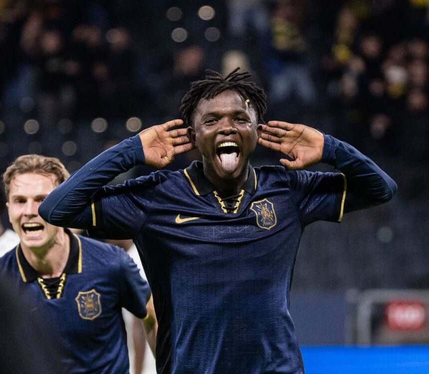 Soccer player in a navy kit celebrates with hands cupping the ears and tongue out on the field  trybalnews