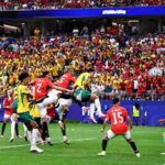 Mohamed Hany of Egypt wearing a red jersey with number 2 attempts a defensive clearance in front of goal during the FIFA World Cup 2026 Round of 32 match between Australia and Egypt at Dallas Stadium in Arlington Texas on July 3 2026 The ball is in the air near the goal line as Australian players in yellow and green and other Egyptian players in red contest a header The score was leveled at 1 1 following an own goal A packed stadium crowd fills the background with DALLAS and FIFAWorldCup visible on the stadium signage  trybalnews