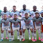 Belgium national team players pose for a team photo before the FIFA World Cup 2026 Round of 16 match against USA at Seattle Stadium in Seattle on July 6 2026 The goalkeeper wears a green kit while outfield players wear light blue and pink patterned away jerseys with white shorts A player holds a red Belgium pennant  trybalnews