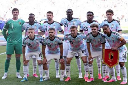 Belgium national team players pose for a team photo before the FIFA World Cup 2026 Round of 16 match against USA at Seattle Stadium in Seattle on July 6, 2026. The goalkeeper wears a green kit while outfield players wear light blue and pink patterned away jerseys with white shorts. A player holds a red Belgium pennant.