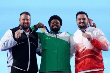 Gold medalist Chukwuebuka Enekwechi of Team Nigeria in green and white tracksuit stands between silver medalist Tom Walsh of New Zealand in black and white and bronze medalist Scott Lincoln of England in red and white, as all three hold up their medals on the podium during the Men's Shot Put Final medal ceremony on Day 7 of the Glasgow 2026 Commonwealth Games at Scotstoun Stadium, July 30, 2026.