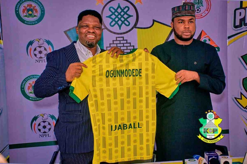 DanielOgunmodede Trybal News New Kano Pillars Technical Adviser Daniel Ogunmodede and Kano Pillars Chairman Alhaji Ahmad Musbahu Garo holding up a yellow and green Kano Pillars jersey with OGUNMODEDE and IJABALL on the back during his official press unveiling Photo Credit Kano Pillars Media trybalnews