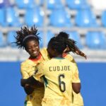 Two soccer players in yellow jerseys hug and celebrate on the field with blue stadium seating behind them one jersey shows the name CUDJOE and number 6  trybalnews