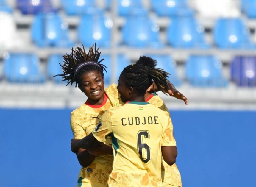 Two soccer players in yellow jerseys hug and celebrate on the field with blue stadium seating behind them one jersey shows the name CUDJOE and number 6  trybalnews